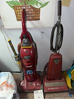 Photo showing two floor cleaning devices: red Eureka carpet cleaner and red vintage Panasonic vacuum cleaner side by side on carpet floor.