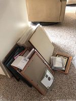 Photo showing multiple picture frames stacked leaning against a wall including various sizes and styles