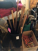 Black bin with various wooden handles for axes or mauls standing upright.