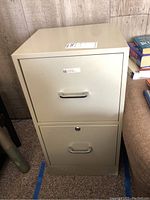 Front view of closed beige two drawer metal file cabinet with metal handles and lock on top drawer.