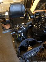 Front view of mobility scooter showing cushioned seat, armrests, handlebar grips, and attached front storage bag.