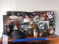 Overview photo showing arrangement of cat and owl figurines, framed cat pictures, a calendar, a floral bag, and cat beach towel.