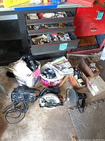 Photo of power tools and hardware on floor near tool drawers including circular saw, buffer, drill, and pet shaver