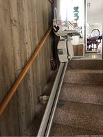 Side view of the stairlift with seat and rail installed on carpeted stairs.