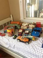 Overall view of painted tin, assorted small cars, orange convertible, blue buggy, forklift and camper trucks on grid-patterned surface