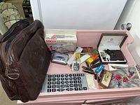 Overview of contents in a pink tray, showing laptop bag, portable music player, boxed watch and pen set, calculator, wallet, and small boxes