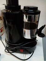 Front-side view showing the glossy black body, chrome grinding container, power switch and attached cord.