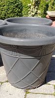 Front view showing detail of one of the black plastic garden planters with diamond pattern and decorative band.
