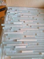 Top view of several glass wall tile pieces showing linear rectangular strip pattern, colors appear clear glass with white rectangular inserts.