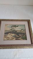 Full view of framed print showing pine trees on rocky terrain with hills under sky.
