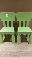Two lime green children's chairs shown side by side on a wooden floor against a brown wall.