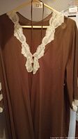Brown sleeveless nightgown hanging on hanger with white lace embroidery along the v-neck neckline