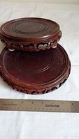Two round wooden planter bases stacked, displaying top surfaces with carved circular patterns and a ruler showing size.