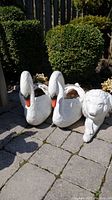 Two white swan-shaped plastic planters with orange and black beaks shown outside on stone paving.