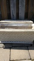 Two images showing a set of two rectangular plastic garden planters with lattice pattern, stacked against a wooden fence on outdoor stone paving. Both planters are beige/off-white with some dirt and weathering.