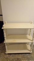 Front view of white wooden shelf with three shelves and turned spindle legs