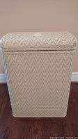 Front view showing light-colored wicker with zigzag pattern and hinged lid closed.