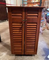 Front view of wooden cabinet bar cart with two louvered doors, metal knobs and lock (lock latch not working).