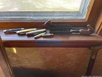 Four pocket carving knives, men's hairbrush, and metal shoe horn displayed on a window ledge.