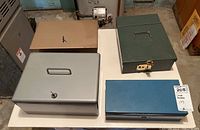 Top-down view of four lock boxes on a white table showing different colors and sizes, keys in some locks, a lock on green box, and tags attached to table.