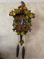 Full view of the cuckoo clock showing the bird carving, leaves, and clock face with Roman numerals.