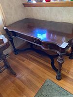 Front angle view of vintage wooden desk showing center drawer, curved front edges, and embellished carved legs