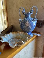 Photo showing the hand-painted Italian urn in blue and white depicting classical figures, placed next to a gold scalloped bowl.