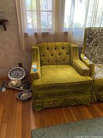 Full view of the green velveteen tufted armchair by the window showing its shape and skirted bottom.
