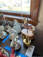 Five music boxes on window ledge including porcelain horses and unicorns, brass horse, and wooden carousel horse.