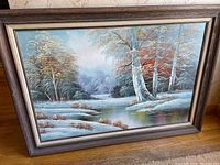 Frontal view of signed oil on canvas painting showing winter landscape of snowy trees and stream inside a wooden frame.