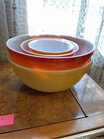Stacked view of four Pyrex bowls showing colors and sizes from largest yellow bowl to smallest orange one, highlighting vintage design.