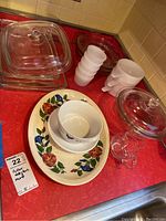 Full view of Pyrex glass lids, bowls, pie plate, milk glass cups, and glazed floral platter on red countertop