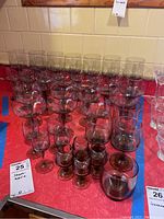 Wide view of assorted tinted stemware and glasses arranged on red surface including several sizes and styles.