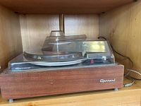 Side view of Garrard turntable showing wooden base and transparent dust cover with Garrard logo visible.