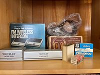 Full lot showing boxed Realistic FM Wireless Intercom, Custom Pro Stereo Headphones box containing headphones wrapped in plastic, Bentley Battery Tester and DC Auto Adapter boxes, and smaller boxes with cartridges and needles.