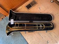 Yamaha trombone inside its open black hard case lined with soft fabric. Case shows wear on exterior.