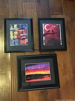 Three framed art prints laid on the floor showing variety of artwork styles.