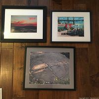 Three framed wall art prints, including a sunset image, beach scene and rock formation, placed on wooden floor