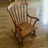 Front angled view of the antique child's rocking chair showing the wood grain, spindle back, and armrests.