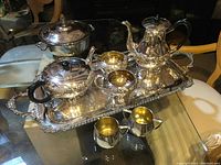 The full tea and coffee set displayed on a glass table with antique furniture in background