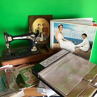 Antique Singer sewing machine and vintage sewing pattern catalogs spread out on green background.