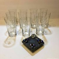Full lot view showing 10 crystal glasses arranged behind a square decorative coaster with beads and central ornamental piece.