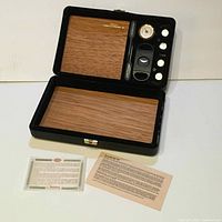 Closed open view of Csonka Cigar Valet humidor showing interior with Spanish cedar liner, several cigar humidification gadgets including a cutter, humidifier, and analog hygrometer on lid, plus documentation cards laid out in front