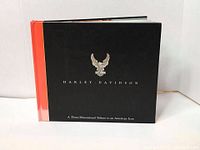 Closed cover of the hardcover Harley-Davidson tribute book with black front and orange spine.