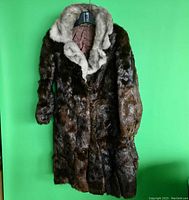 Front view of the long mink fur coat hanging against a green background showing dark brown fur with beige-gray fur collar and cuffs.