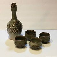 Full set photo showing one bottle and four cups, all with green and brown glaze.