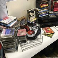 Overview photo showing stacks of DVDs, CDs, silver Panasonic player, black Motorola DVD player, and media storage items on table