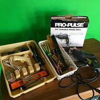 Photo showing Pro Pulse electric drill, its box, hot glue gun, tape measure, level, pliers, and screwdrivers in plastic trays on table