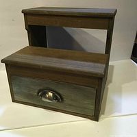 Front view of wooden two-step stool showing drawer with metal handle.