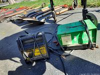 Two battery chargers outside on pavement with grass in background, one green Sears charger with cables and clamps coiled on top, one smaller black charger next to it.